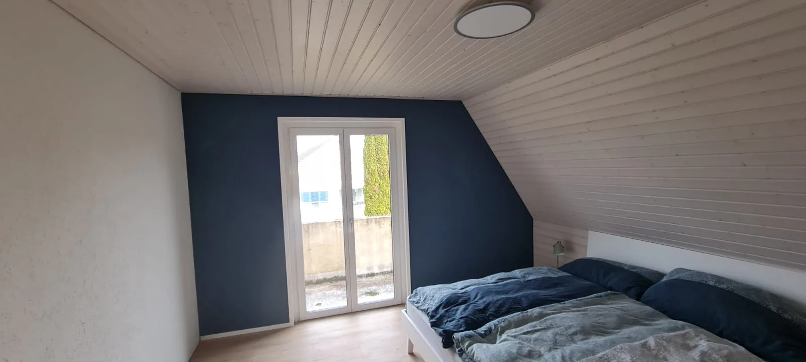 Schlafzimmer mit dunkelblauer Akzentwand und weisser Holzdeckenverkleidung nach Malerarbeiten